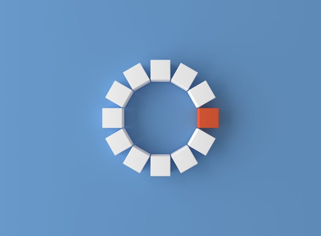 A minimalist 3D render featuring a circle of white cubes with one red cube on a blue background.